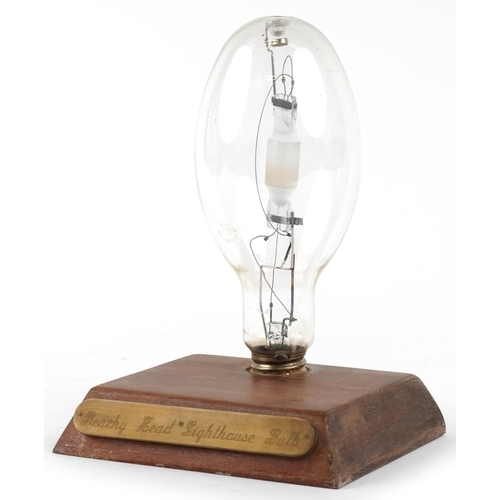 A late 20th century Beachy Head Lighthouse bulb, mounted on a stained pine plinth with inscribed plaque, 30cm H x 22cm W x 17cm D.