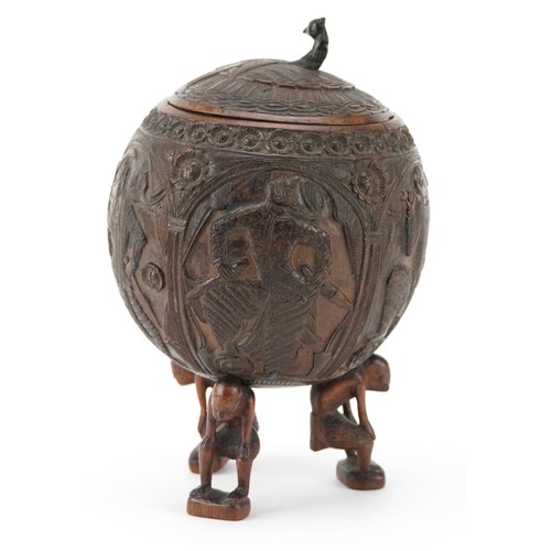 58 - A late 19th century Indian coconut tea caddy carved in relief with warriors and raised on three figu... 