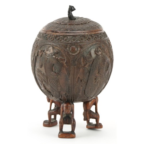 58 - A late 19th century Indian coconut tea caddy carved in relief with warriors and raised on three figu... 