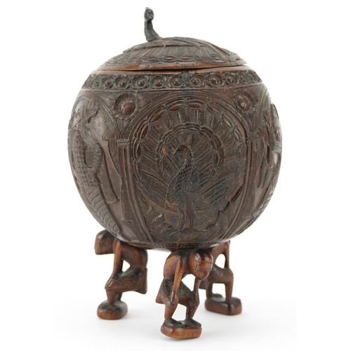 58 - A late 19th century Indian coconut tea caddy carved in relief with warriors and raised on three figu... 