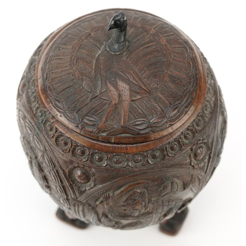58 - A late 19th century Indian coconut tea caddy carved in relief with warriors and raised on three figu... 