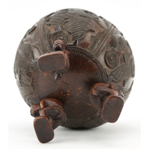 58 - A late 19th century Indian coconut tea caddy carved in relief with warriors and raised on three figu... 