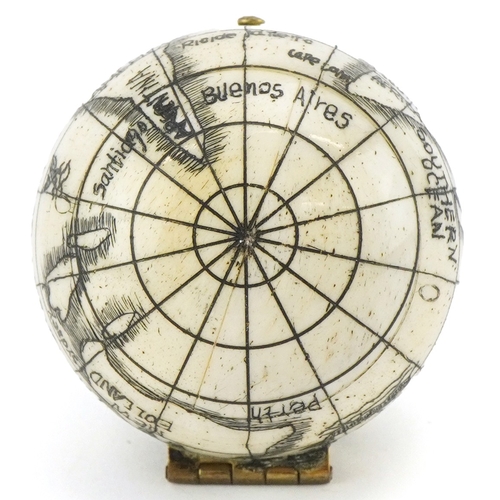 49 - A scrimshaw style etched bone compass in the form of a globe, 4cm in diameter.