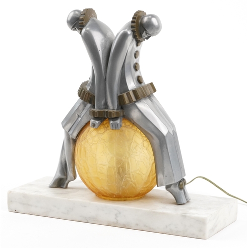 An Art Deco aluminium and glass Pierrot figural table lamp with amber frosted glass shade, raised on a marble base, 30cm high.