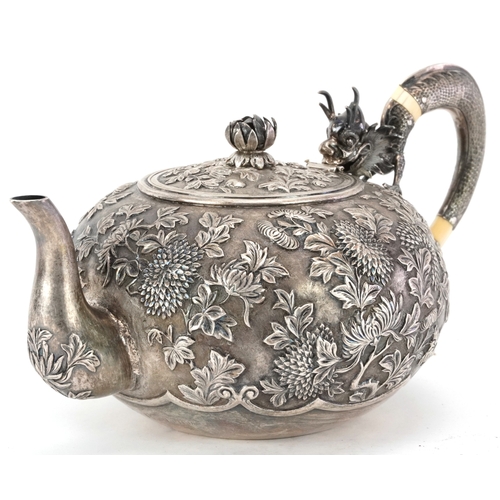 A Chinese export silver teapot, the handle in the form of a dragon, profusely embossed with flowers and foliage, character marks to the base, 25cm in length, 618.0g.