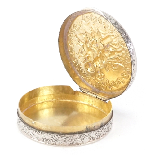 52 - A silver circular snuff box embossed with Putti, London import marks 1976, 5.3cm in diameter, 35.8g.