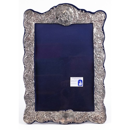 39 - Henry Matthews, a very large silver easel photo frame profusely embossed with flowers, foliage and a... 