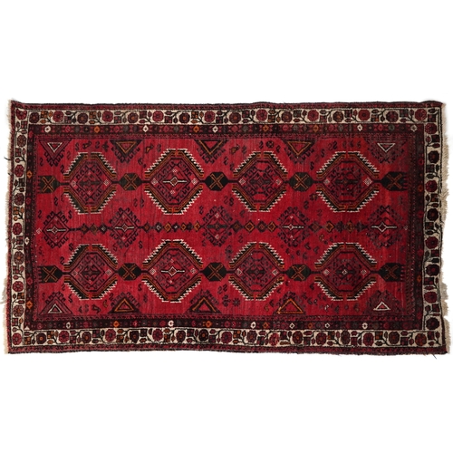 2223 - An Afghan rug, 20th century, the red field with two rows of stylized medallions within a complementa... 