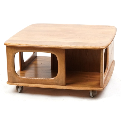 1010 - An Ercol elm square coffee table fitted with a drawer and open shelves, on casters, 41cm H x 78cm W ... 