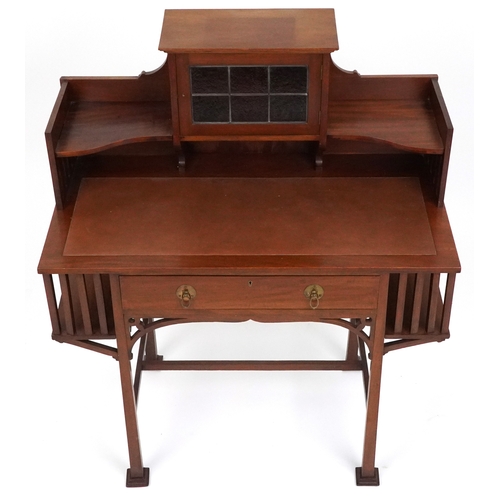  An Arts & Crafts mahogany desk, the shelf back with a leaded glass door above a frieze drawer, raise... 