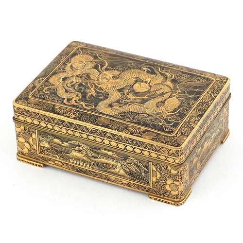 Fine Japanese brass damascene box having hinged lid, finely inlaid with 24K gold depicting a dragon amongst clouds, birds of paradise and buildings, 4cm H x 10.5cm W x 7.5cm D.