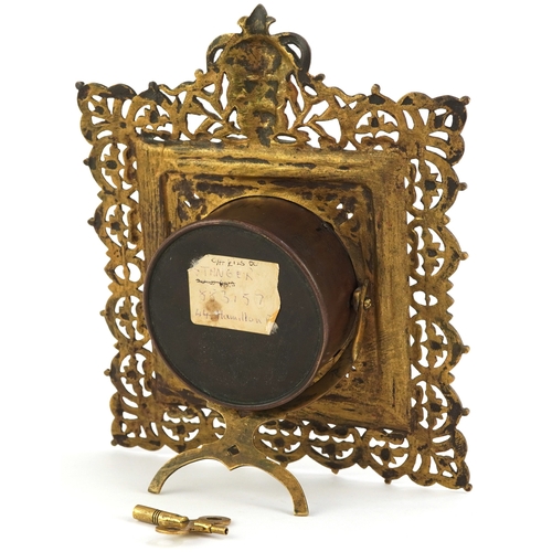 214 - Antique brass strut clock embossed with masks and engraved with fish, the enamelled dial having Roma... 