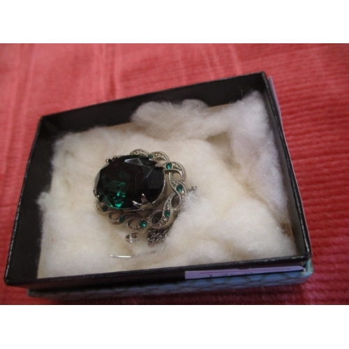 52 - SILVER COLOURED BROOCH WITH LARGE GREEN STONE TO THE CENTRE AND OPEN TWISTED DESIGN TO EDGE WITH SMA... 