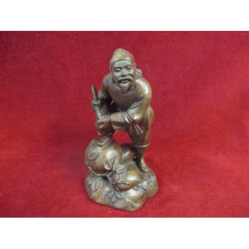 184A - 20TH CENTURY ORIENTAL CARVED WOOD FIGURE OF A MAN ON ROCKS WITH TRAILING LEAVES - 21CM