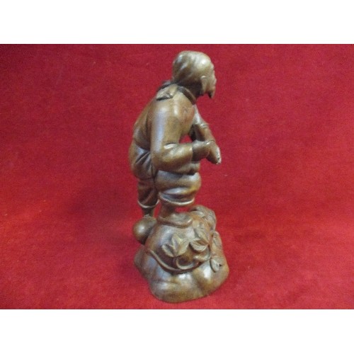 184A - 20TH CENTURY ORIENTAL CARVED WOOD FIGURE OF A MAN ON ROCKS WITH TRAILING LEAVES - 21CM