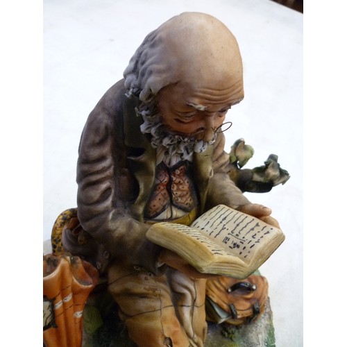 223 - A LARGE CAPODIMONTE FIGURE OF AN OLD GENTLEMAN READING ON A BENCH - SIGNED ON THE BACK 