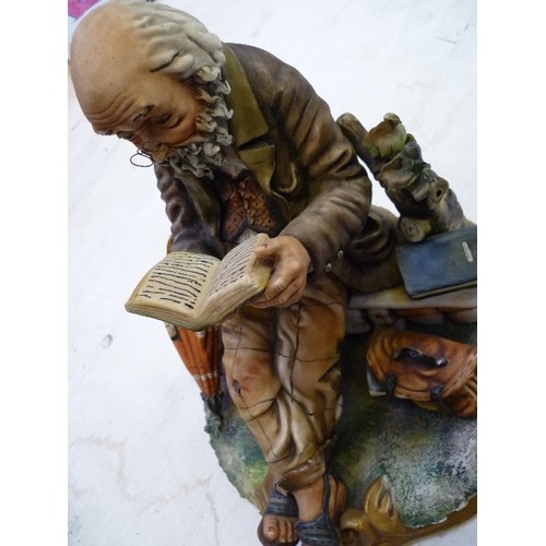 223 - A LARGE CAPODIMONTE FIGURE OF AN OLD GENTLEMAN READING ON A BENCH - SIGNED ON THE BACK 