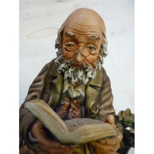 223 - A LARGE CAPODIMONTE FIGURE OF AN OLD GENTLEMAN READING ON A BENCH - SIGNED ON THE BACK 