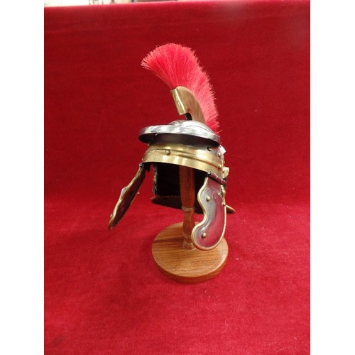 118 - A WELL MADE ROMAN CENTURION MINIATURE HELMET ON A WOODEN STAND - TOTAL HEIGHT WITH STAND 28CM