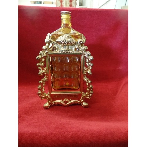 67 - AMBER COLOURED GLASS DECANTER IN WIND UP MUSICAL GILT METAL CLOCK STYLE FRAME