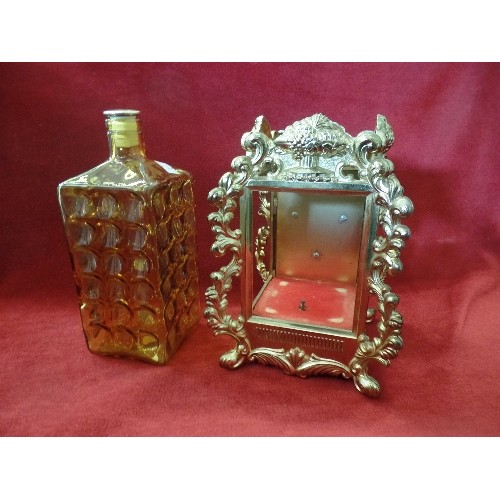 67 - AMBER COLOURED GLASS DECANTER IN WIND UP MUSICAL GILT METAL CLOCK STYLE FRAME