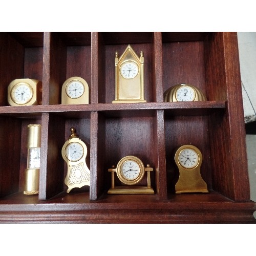 202 - 24 MINIATURE BRASS CLOCKS IN A WOODEN DISPLAY CASE