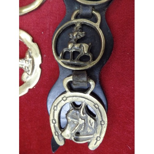 125 - 7 X SMALL VINTAGE HORSE BRASSES ON A BLACK LEATHER STRAP, ALSO 4 LOOSE BRASSES.