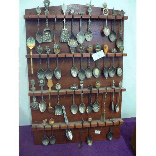 125 - LARGE COLLECTION OF SOUVENIR SPOONS DISPLAYED ON WOODEN WALL RACK.