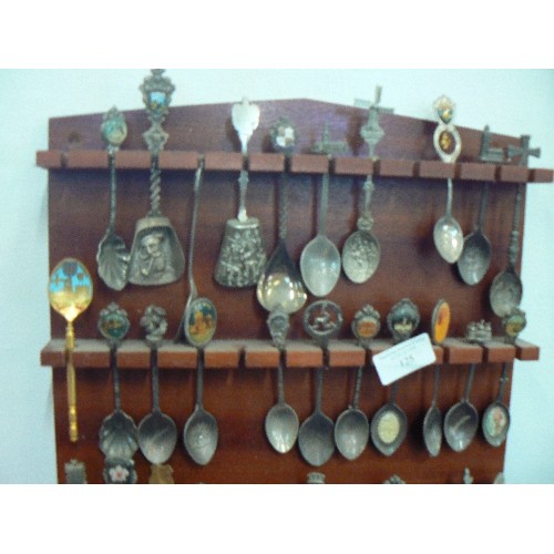 125 - LARGE COLLECTION OF SOUVENIR SPOONS DISPLAYED ON WOODEN WALL RACK.