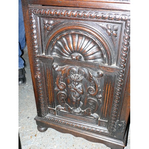 433 - Early to mid 20th Century oak cupboard with drawer, the door deeply carved with a cherub playing a t... 