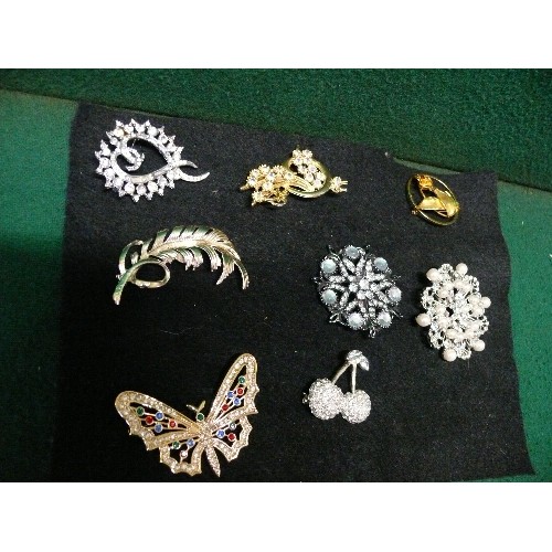 25 - EIGHT BROOCHES ADORNED IN STONES AND GEMS DISPLAYED ON FELT.