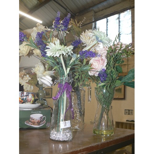 387 - THREE CLEAR VASES WITH ARTIFICIAL FLOWERS.