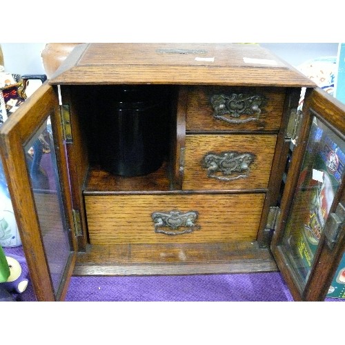 112 - ANTIQUE OAK SMOKERS CABINET  WITH TWO BEVEL EDGED GLASS DOORS CONCEALING  THREE DRAWERS AND BLUE TOB... 