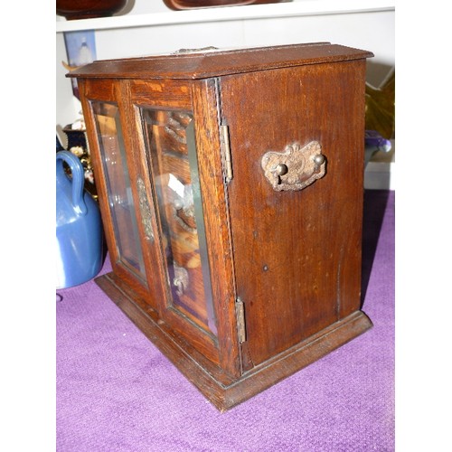 112 - ANTIQUE OAK SMOKERS CABINET  WITH TWO BEVEL EDGED GLASS DOORS CONCEALING  THREE DRAWERS AND BLUE TOB... 