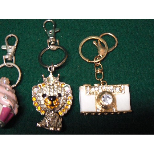 46 - FOUR NOVELTY KEY RINGS ENCRUSTED IN BLINGY STONES -  CAMERA, LION, CUP CAKE, PLUS ONE OTHER.