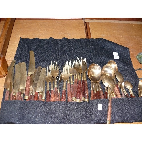 256 - A LARGE WOOD AND BRASS CUTLERY SET IN A ROLL-UP CASE.