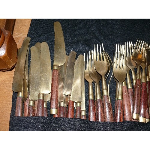 256 - A LARGE WOOD AND BRASS CUTLERY SET IN A ROLL-UP CASE.