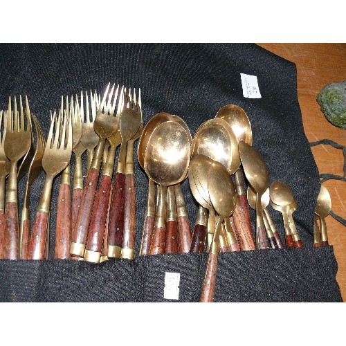 256 - A LARGE WOOD AND BRASS CUTLERY SET IN A ROLL-UP CASE.