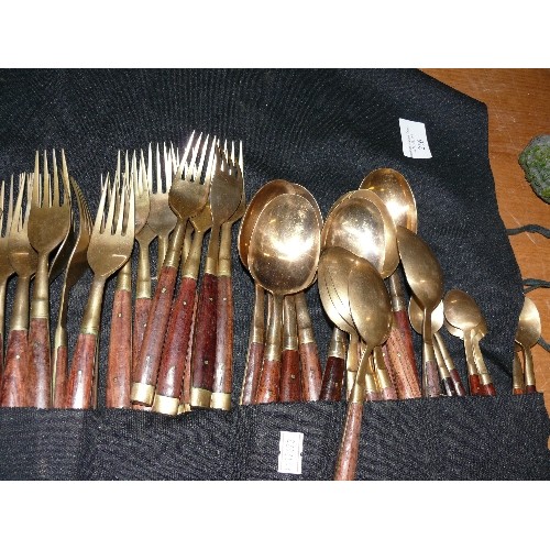 256 - A LARGE WOOD AND BRASS CUTLERY SET IN A ROLL-UP CASE.