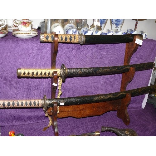 134 - A SET OF THREE ORNAMETAL SAMURAI SWORDS ON STAND.