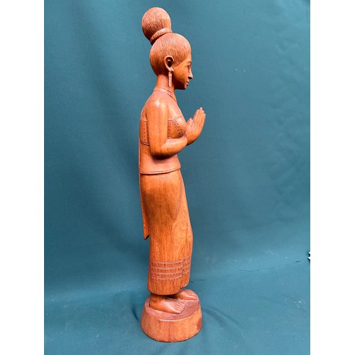 134 - A tall Balinese hand carved wooden figure of a woman in traditional dress. 60cm