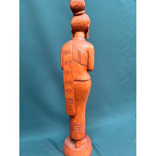 134 - A tall Balinese hand carved wooden figure of a woman in traditional dress. 60cm