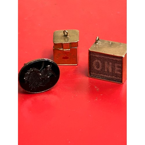 59 - Three 9ct gold charms including a First Aid Box, a sealed £1.00 note and a fob seal with carved blac... 