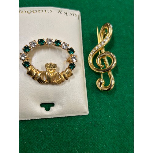 41 - TWO BROOCHES INCLUDING A TREBLE CLEF MUSIC NOTE AND A HAND & HEART BROOCH WITH EMERALD COLOUR & CLEA... 