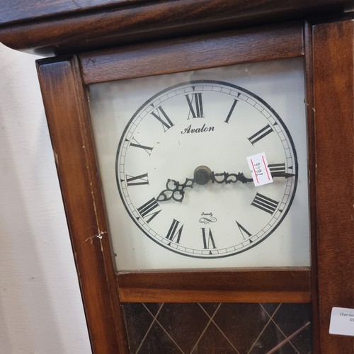 94 - A SMALL AVALON WALL CLOCK IN NICE WOODEN CASE WITH ROMAN NUMERALS IN A CREAM FACE WITH PENDULUM.