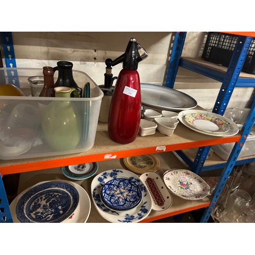 358 - 3 SHELVES OF CERAMICS AND GLASSWARE, SODA SYPHON, PLATTERS, STONEWARE BOTTLES, GLASS LAMPSHADES ETC