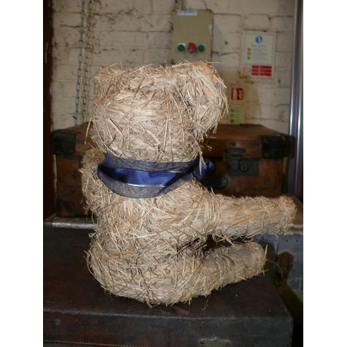 410 - A straw teddy bear wearing a blue ribbon. 35cm tall.