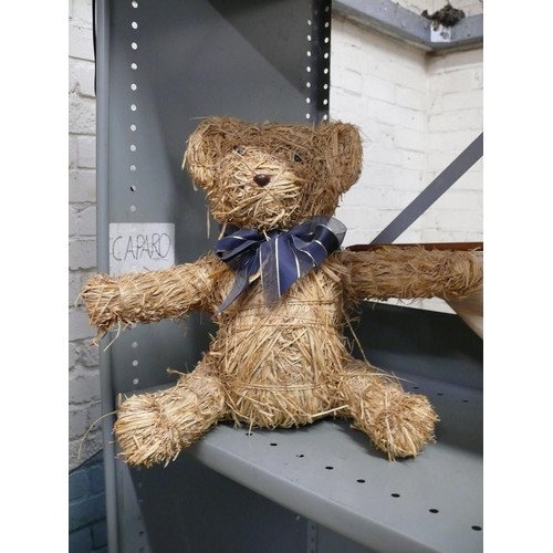 410 - A straw teddy bear wearing a blue ribbon. 35cm tall.