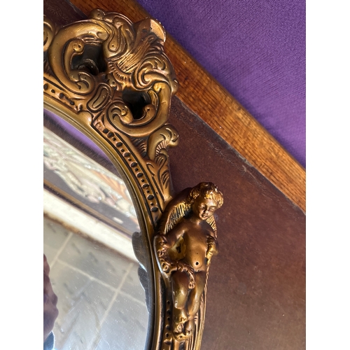 231 - Vintage gilt framed oval wall mirror in the rococo style with four cherubs adorning the frame. 64cm ... 