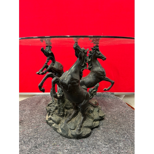 599 - A 20th Century circular glass topped coffee table with the base in the form of three rearing horses.... 